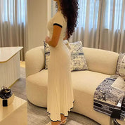 Abito lungo bianco a coste, maniche corte, indossato da donna in salotto moderno. Design elegante, perfetto per moda estiva e occasioni casual.