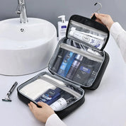 Astuccio da viaggio nero aperto con prodotti per l'igiene maschile, appeso vicino a un lavandino bianco. Include shampoo, deodorante e rasoio.