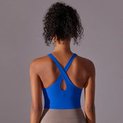 Donna di spalle indossa top sportivo blu con spalline incrociate, ideale per yoga e fitness. Abbigliamento sportivo donna, comfort e stile.