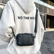 Zaino nero in stile urbano indossato su felpa bianca con scritta "NO TIME NO S", ambientato in contesto cittadino moderno.