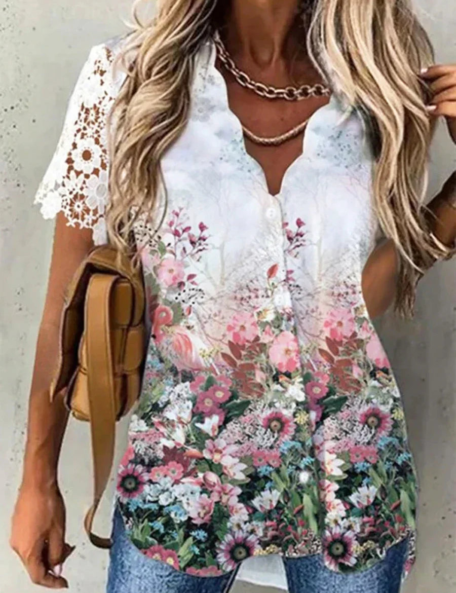 Blusa donna floreale estiva, maniche corte in pizzo bianco, bottoni frontali, colori vivaci, abbinata a jeans e borsa marrone.