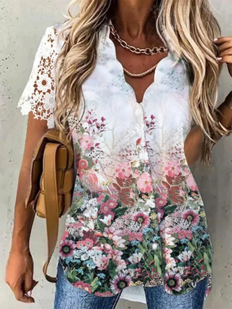 Blusa donna floreale estiva, maniche corte in pizzo bianco, bottoni frontali, colori vivaci, abbinata a jeans e borsa marrone.