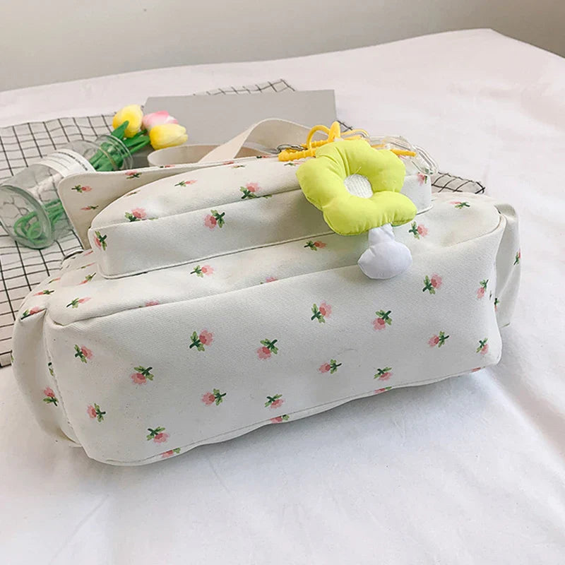 Borsa a tracolla bianca con stampa floreale rosa, decorata con ciondolo giallo. Design elegante e femminile, perfetta per la moda casual.