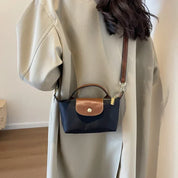 Borsa a tracolla nera e marrone in pelle, indossata su cappotto beige. Design elegante e compatto, ideale per moda autunnale e invernale.