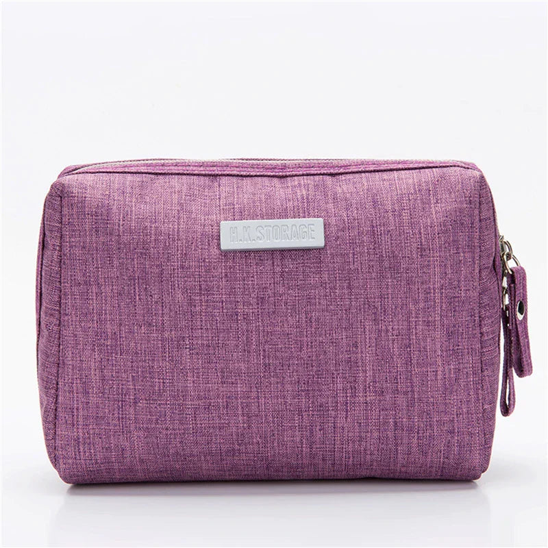 Astuccio da viaggio viola in tessuto, con chiusura a zip e etichetta frontale. Ideale per organizzare accessori e cosmetici.
