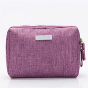 Astuccio da viaggio viola in tessuto, con chiusura a zip e etichetta frontale. Ideale per organizzare accessori e cosmetici.