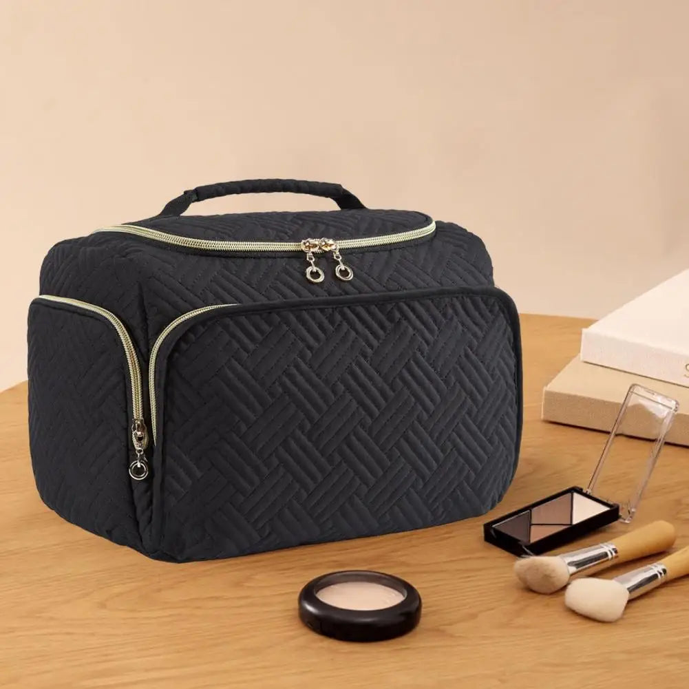 Borsa cosmetica nera trapuntata con cerniera, manico superiore, su tavolo di legno. Include pennelli trucco e palette ombretti. Accessori bellezza.