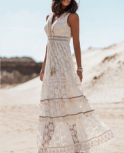 Abito lungo estivo bianco in pizzo, senza maniche, indossato da donna su spiaggia sabbiosa. Stile boho chic, ideale per moda estiva e vacanze.