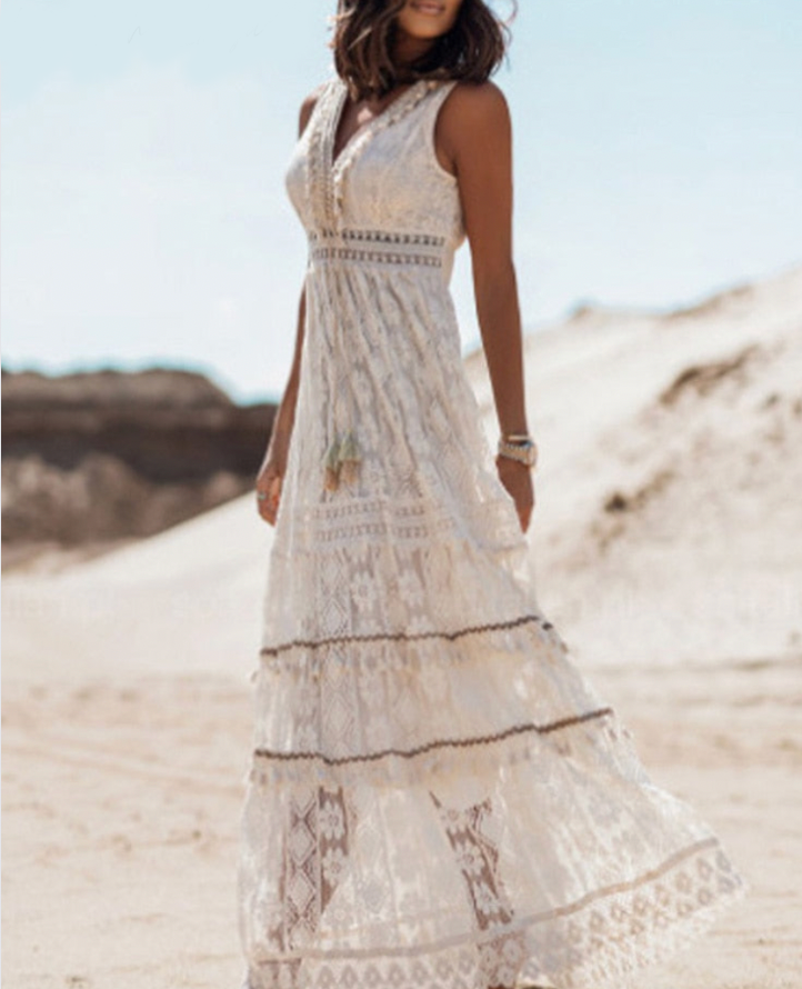 Abito lungo estivo bianco in pizzo, senza maniche, indossato da donna su spiaggia sabbiosa. Stile boho chic, ideale per moda estiva e vacanze.