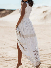 Donna con abito lungo bianco in pizzo, senza maniche, su spiaggia sabbiosa. Moda estiva elegante, abbigliamento femminile boho chic.