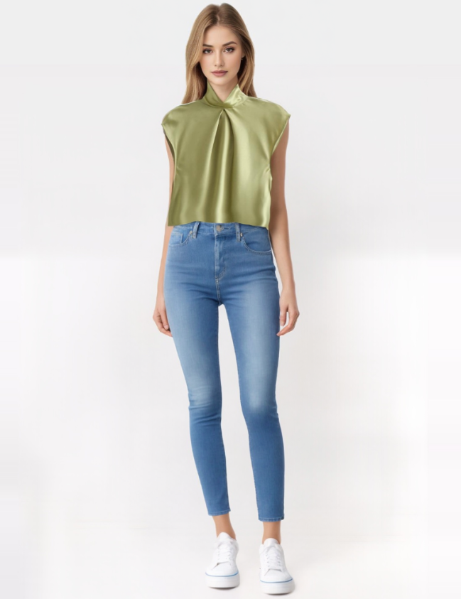 Modella indossa top verde satinato senza maniche e jeans skinny blu, scarpe bianche. Moda donna, abbigliamento casual chic, tendenze 2023.