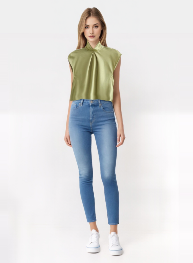 Modella indossa top verde satinato senza maniche e jeans skinny blu, scarpe bianche. Moda donna, abbigliamento casual chic, tendenze 2023.
