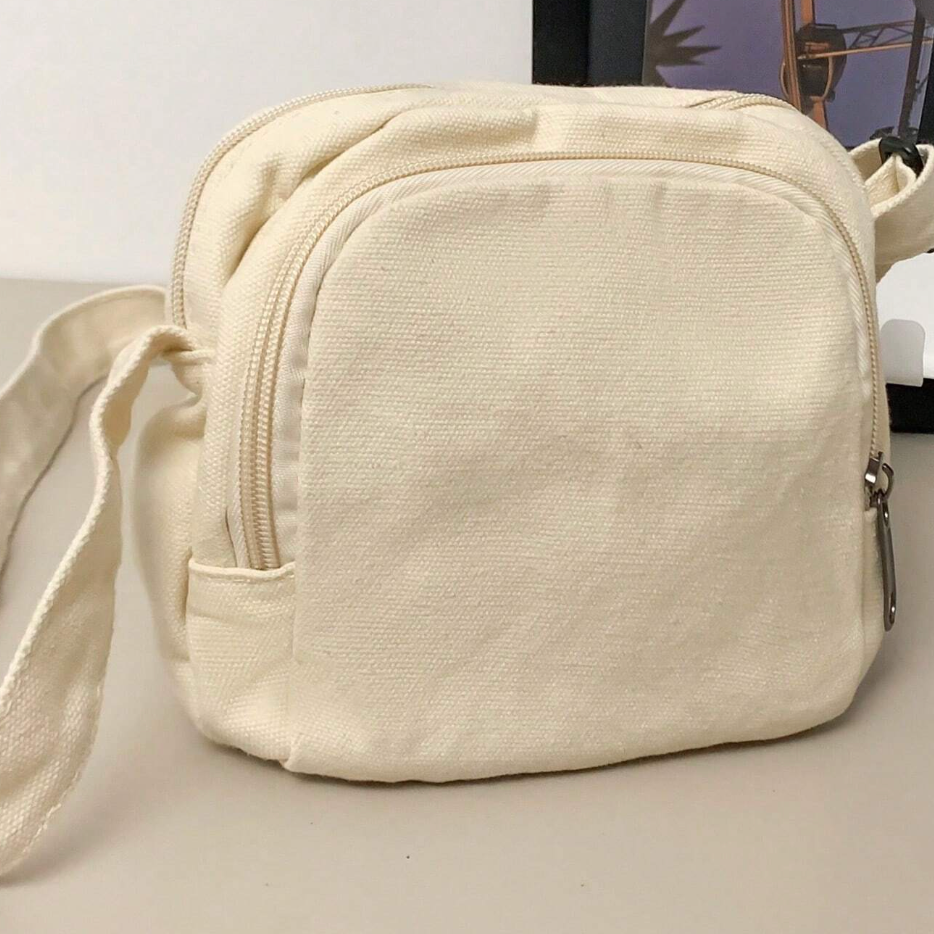Borsa a tracolla in tela beige, design compatto con cerniera, ideale per uso quotidiano. Accessorio moda pratico e versatile.