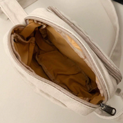 Marsupio beige aperto con cerniera, interno foderato in tessuto marrone chiaro. Accessorio moda unisex, pratico per viaggi e attività all'aperto.