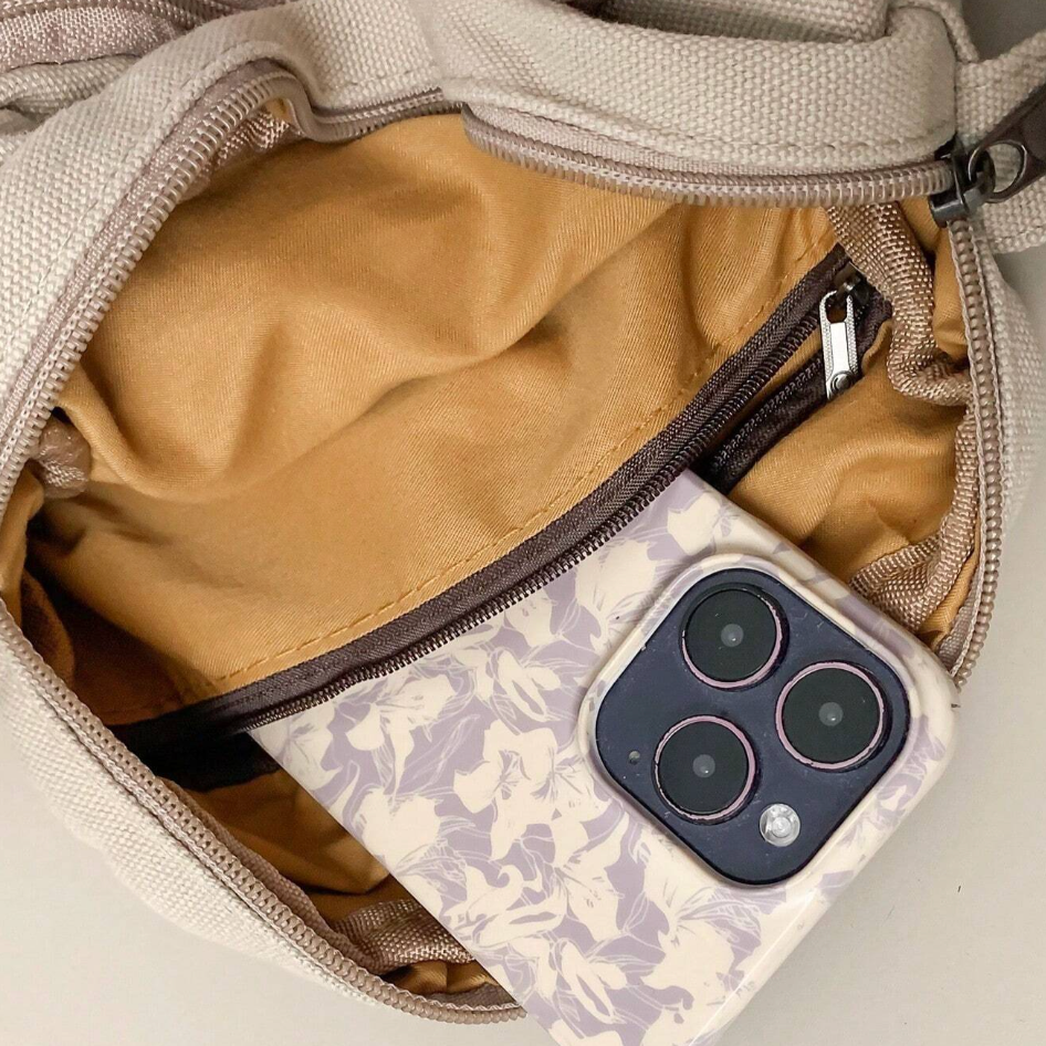 Borsa beige aperta con interno marrone, contenente uno smartphone con cover floreale. Accessorio moda, tecnologia, borsa donna, smartphone moderno.
