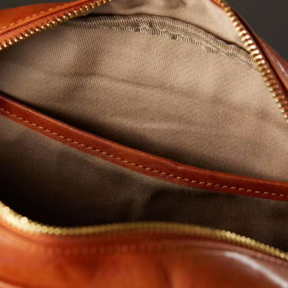 Interno borsa in pelle marrone con cerniera dorata, fodera in tessuto beige. Accessorio moda elegante, alta qualità artigianale.