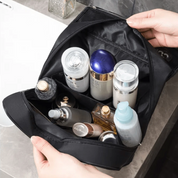 Borsa da toilette nera aperta con flaconi di cosmetici e prodotti per la cura della pelle su un lavandino in bagno. Accessori viaggio essenziali.