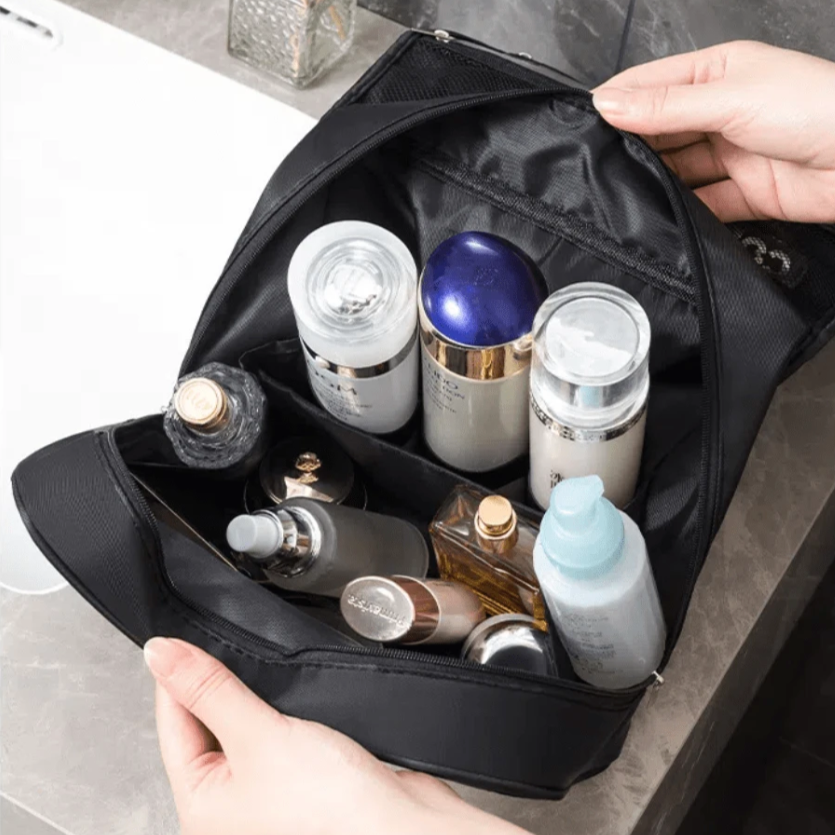 Borsa da toilette nera aperta con flaconi di cosmetici e prodotti per la cura della pelle su un lavandino in bagno. Accessori viaggio essenziali.