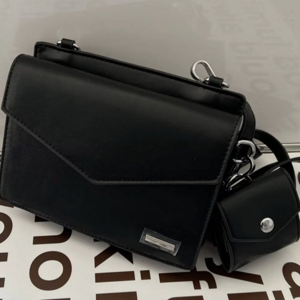 Borsa a tracolla nera elegante in pelle con chiusura a patta, dettagli metallici argentati e mini pochette abbinata. Accessorio moda donna.