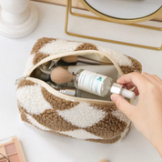 Borsa trucco in tessuto a scacchi beige e bianco, contenente pennelli e flacone di siero. Accessori cosmetici, beauty case elegante.