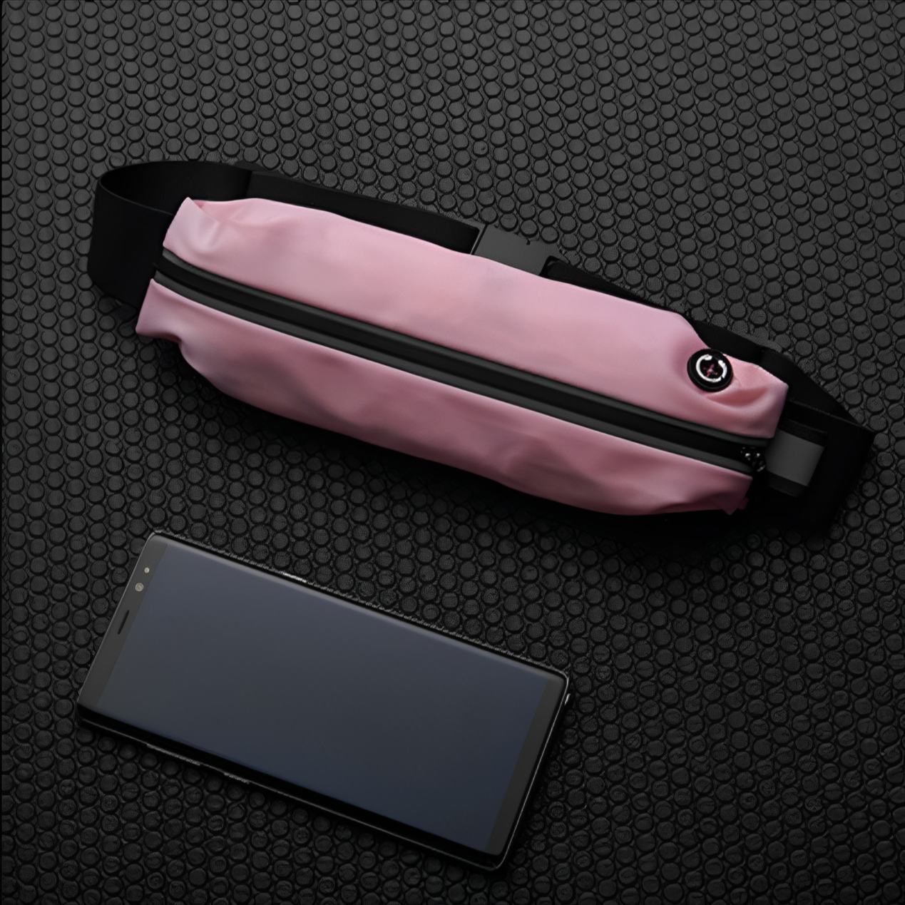 Marsupio rosa impermeabile con cerniera nera, cinturino regolabile, accanto a uno smartphone su sfondo nero a trama esagonale.