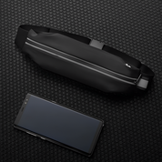 Marsupio nero impermeabile con cerniera riflettente su sfondo a nido d'ape, accanto a smartphone nero. Accessorio moda pratico e moderno.