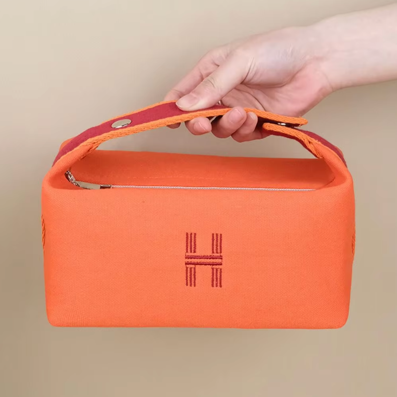 Borsa arancione in tessuto con manico rosso, chiusura a zip e logo ricamato. Design elegante e pratico, ideale per moda e accessori di lusso.
