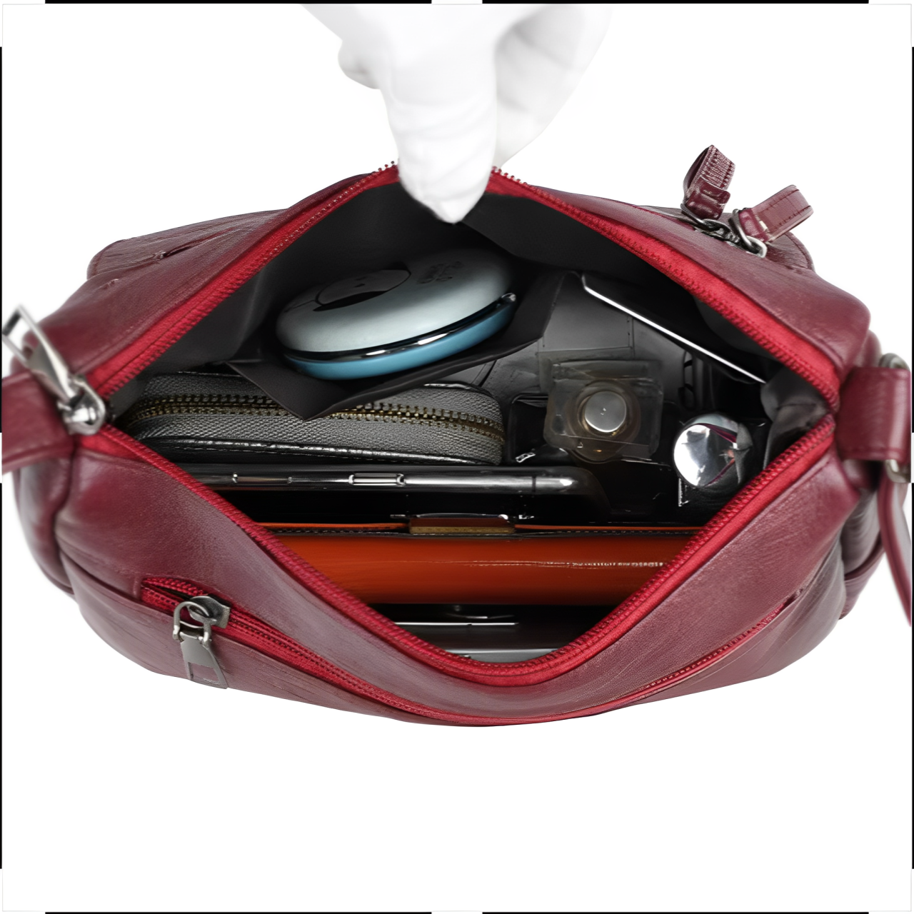 Borsa a tracolla rossa in pelle aperta, contenente portafoglio, trucco, penne e accessori. Design elegante, ideale per moda femminile e praticità quotidiana.