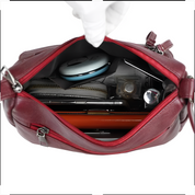 Borsa a tracolla rossa in pelle aperta, contenente portafoglio, trucco, penne e accessori. Design elegante, ideale per moda femminile e praticità quotidiana.