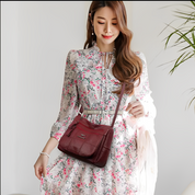 Donna con abito floreale e borsa a tracolla in pelle bordeaux, moda femminile elegante, accessori di tendenza, stile primaverile.