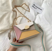 Borsa a tracolla multicolore in pelle con catena dorata, manico superiore e chiusura a scatto. Design geometrico moderno su sfondo bianco.