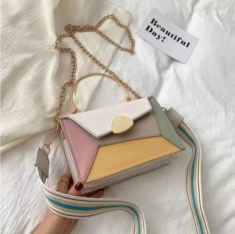 Borsa a tracolla multicolore in pelle con catena dorata, manico superiore e chiusura a scatto. Design geometrico moderno su sfondo bianco.