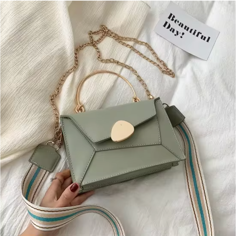 Borsa a tracolla verde salvia con manico dorato e catena, design geometrico, su tessuto bianco. Accessorio moda elegante e moderno.