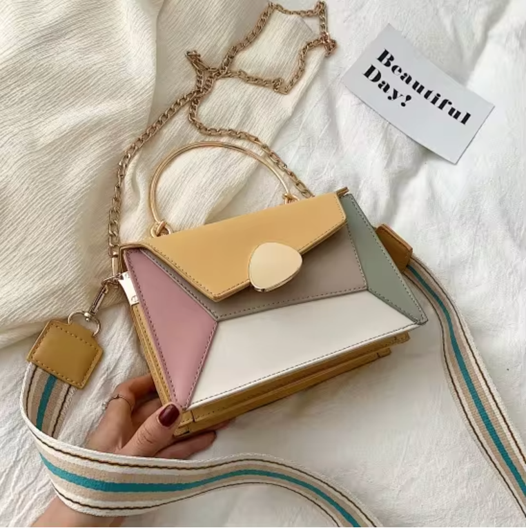 Borsa a tracolla multicolore in pelle con catena dorata, design geometrico, manico superiore e tracolla regolabile su sfondo bianco.