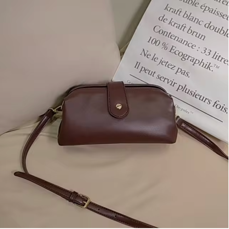 Borsa a tracolla in pelle marrone su divano beige, design elegante con chiusura a bottone. Accessorio moda donna, stile classico e versatile.
