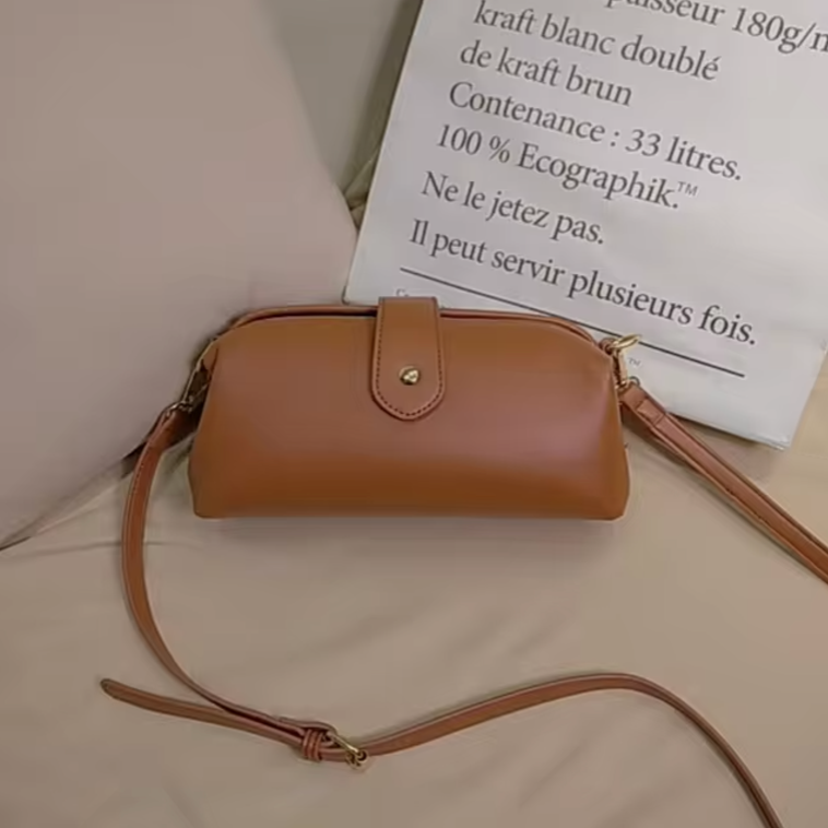Borsa a tracolla in pelle marrone chiaro su letto beige, design elegante con chiusura a bottone dorato, ideale per moda donna e accessori casual.