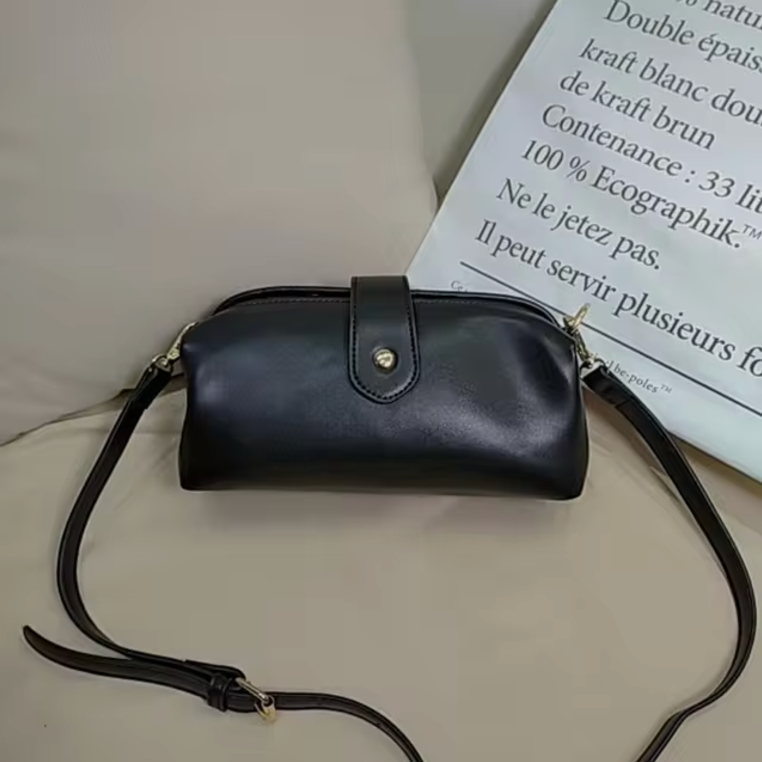 Borsa a tracolla in pelle nera su sfondo beige, design elegante con chiusura a bottone dorato, ideale per moda donna e accessori di lusso.
