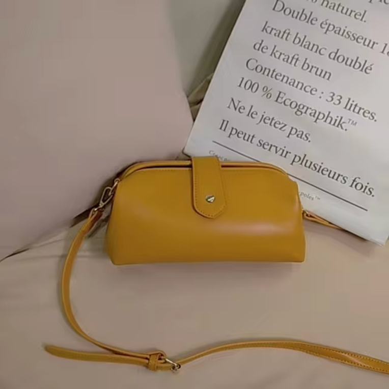 Borsa a tracolla gialla in pelle su divano beige, design elegante e compatto, ideale per moda donna. Accessorio trendy per ogni occasione.