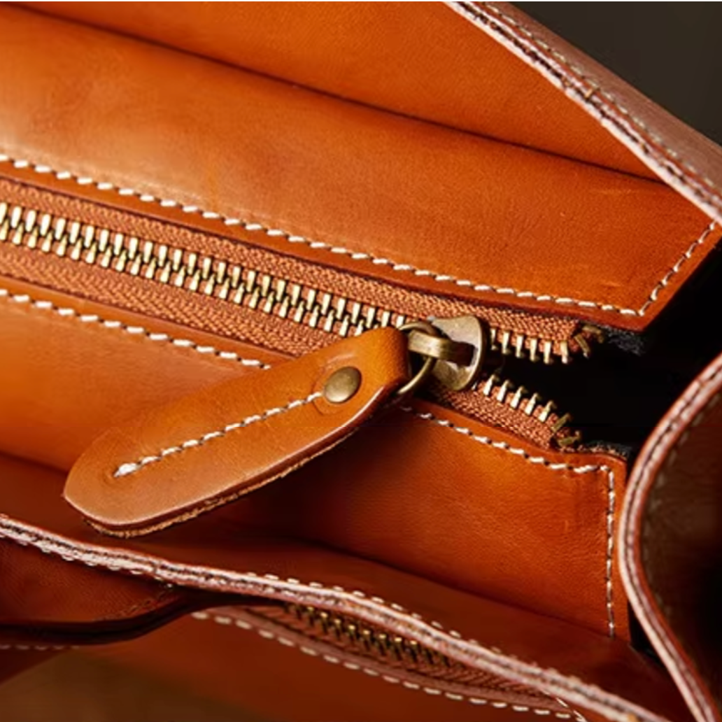 Portafoglio in pelle marrone con cerniera dorata, cuciture bianche a contrasto, design elegante e funzionale, accessorio moda di alta qualità.