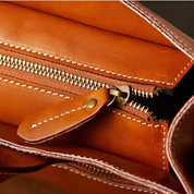 Portafoglio in pelle marrone con cerniera dorata, cuciture bianche a contrasto, design elegante e funzionale, accessorio moda di alta qualità.