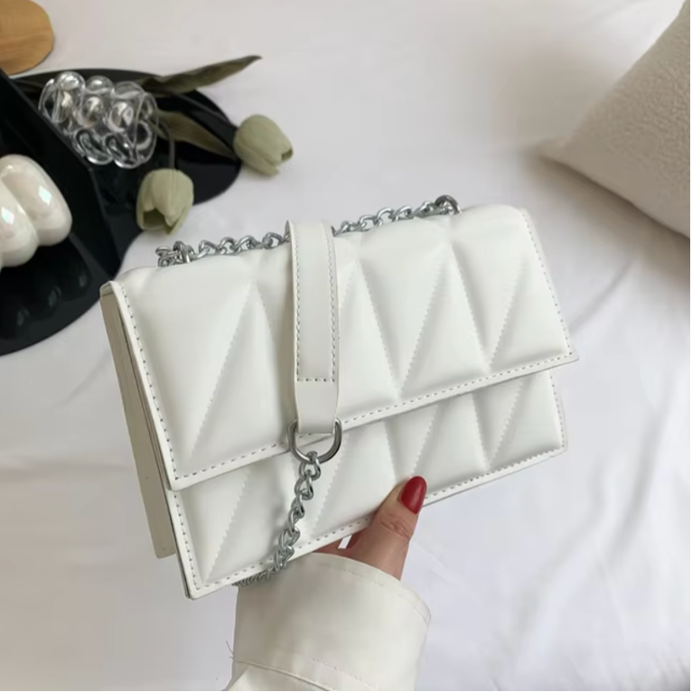 Borsa a tracolla bianca trapuntata con catena argentata, design elegante su sfondo neutro. Accessorio moda donna, stile moderno e chic.