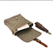 Borsa a tracolla in tela cerata verde con chiusura a bottone, tasca interna per smartphone e tracolla regolabile marrone. Accessorio moda unisex.