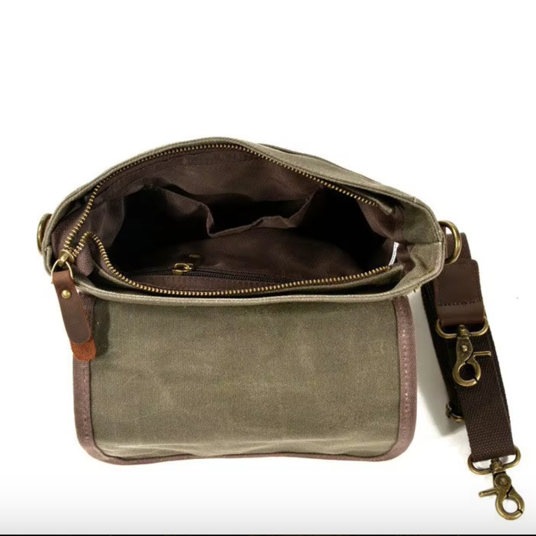 Borsa a tracolla in tela verde oliva con cerniera aperta, tasche interne, tracolla regolabile marrone e dettagli in pelle. Accessorio moda casual.