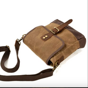 Borsa a tracolla in tela marrone con dettagli in pelle, fibbia in metallo e tasca frontale. Design vintage, ideale per uomo e donna.