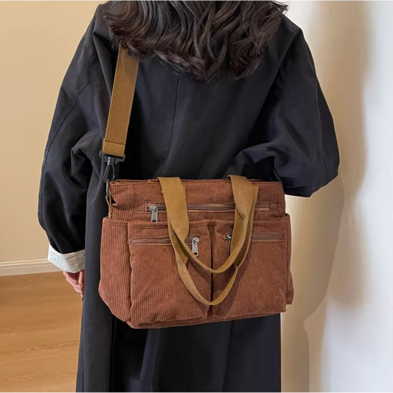 Donna con cappotto nero indossa borsa a tracolla marrone in velluto a coste, tasche con zip, manici corti. Stile casual, moda autunno inverno.