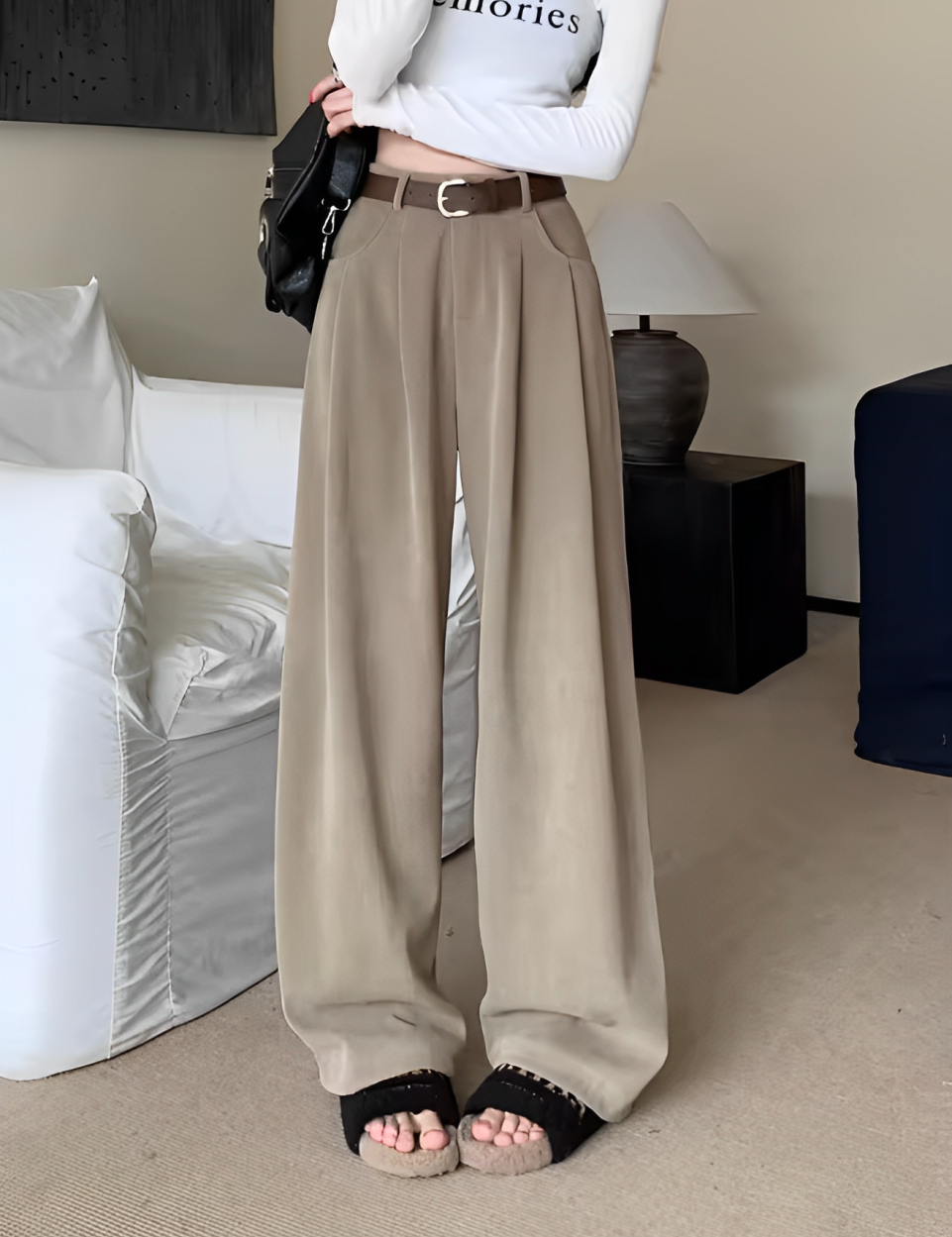 Pantaloni palazzo beige eleganti, abbinati a sandali neri e maglia bianca, in un salotto moderno. Moda donna, abbigliamento casual chic.