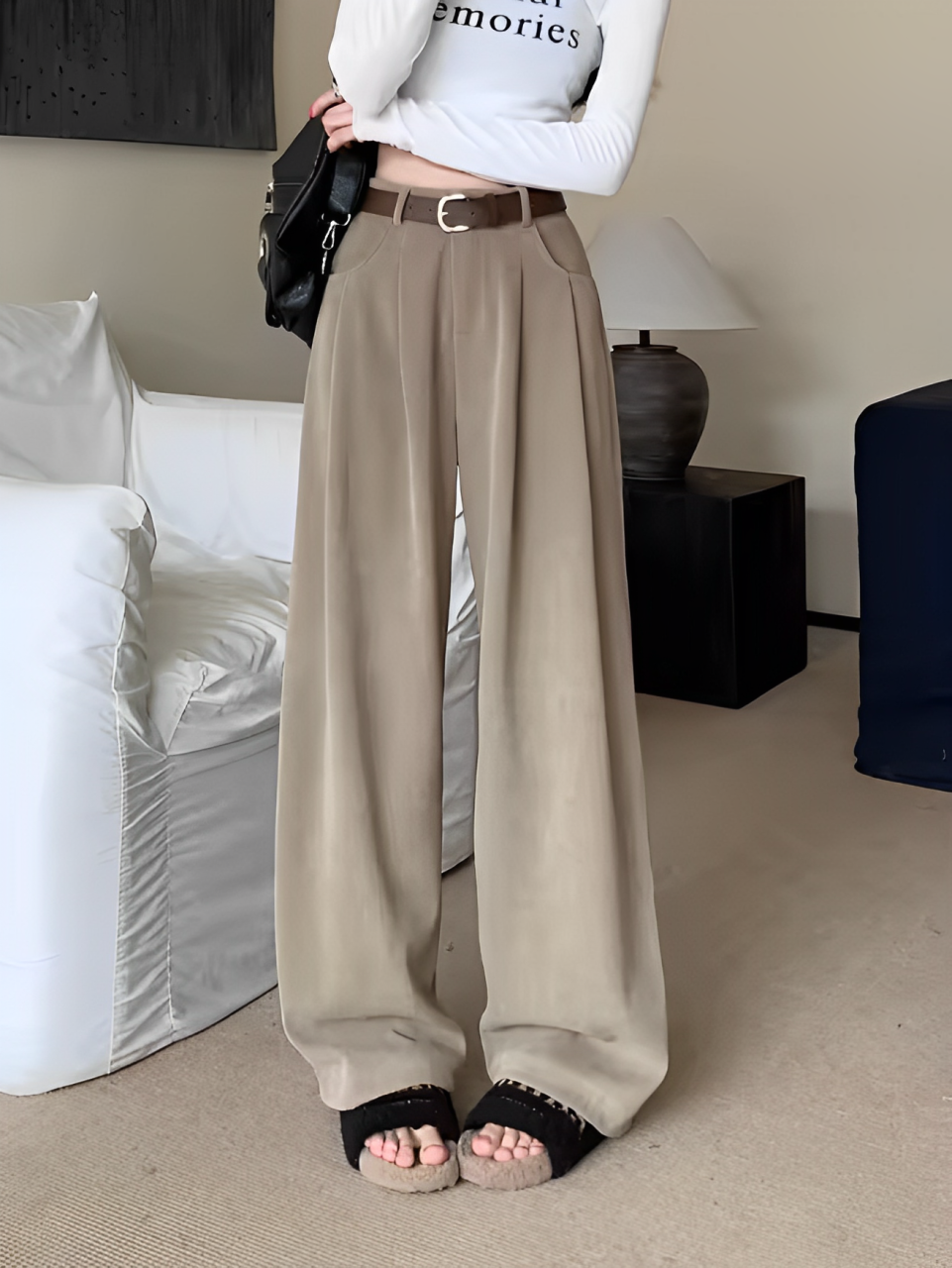 Pantaloni palazzo beige eleganti, abbinati a sandali neri e maglia bianca, in un salotto moderno. Moda donna, abbigliamento casual chic.