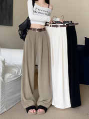 Donna con top bianco e pantaloni beige, tiene due paia di pantaloni su grucce, uno bianco e uno nero. Moda femminile, abbigliamento casual elegante.