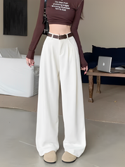 Donna con pantaloni bianchi larghi, cintura marrone e top marrone a maniche lunghe. Stile moda casual, soggiorno moderno.