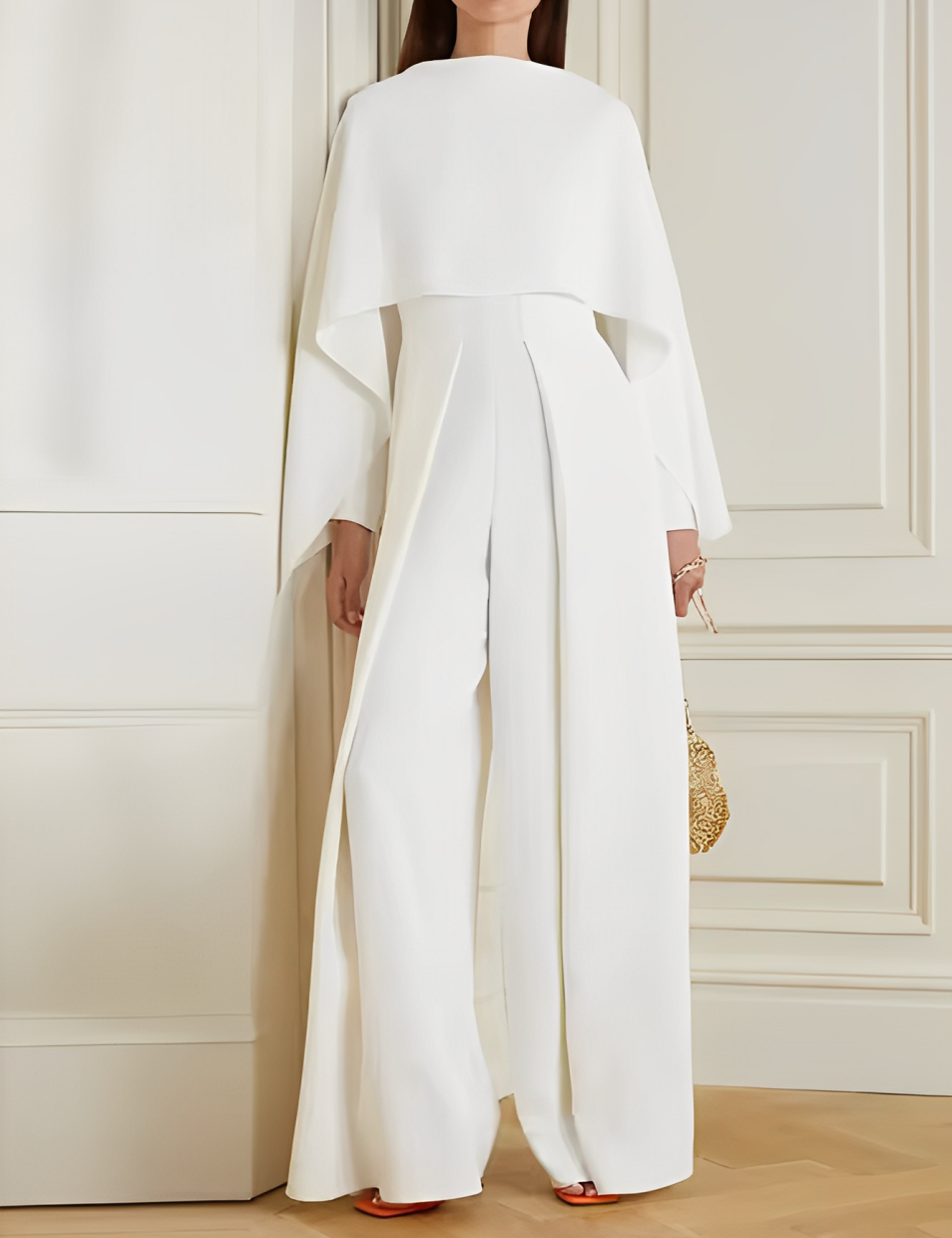 Tuta elegante bianca da donna con mantella, design moderno, indossata in interni. Perfetta per eventi formali e cerimonie.